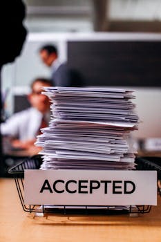 Pile of papers with 'Accepted' label in a busy office setting, highlighting information management.