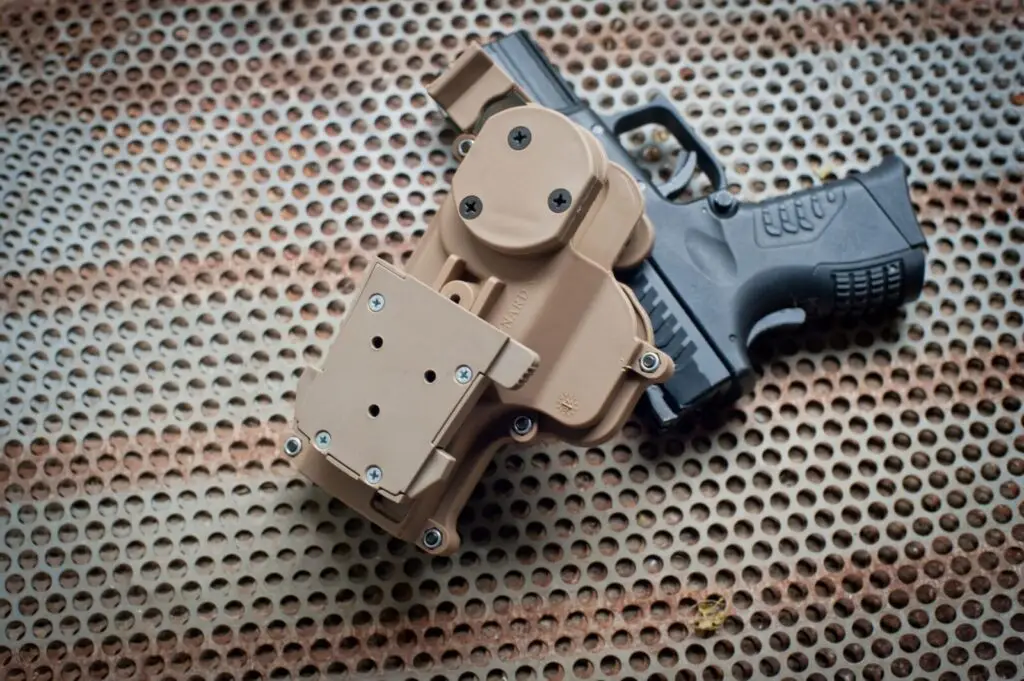 Close-up of a holstered black pistol placed on a perforated metal surface.