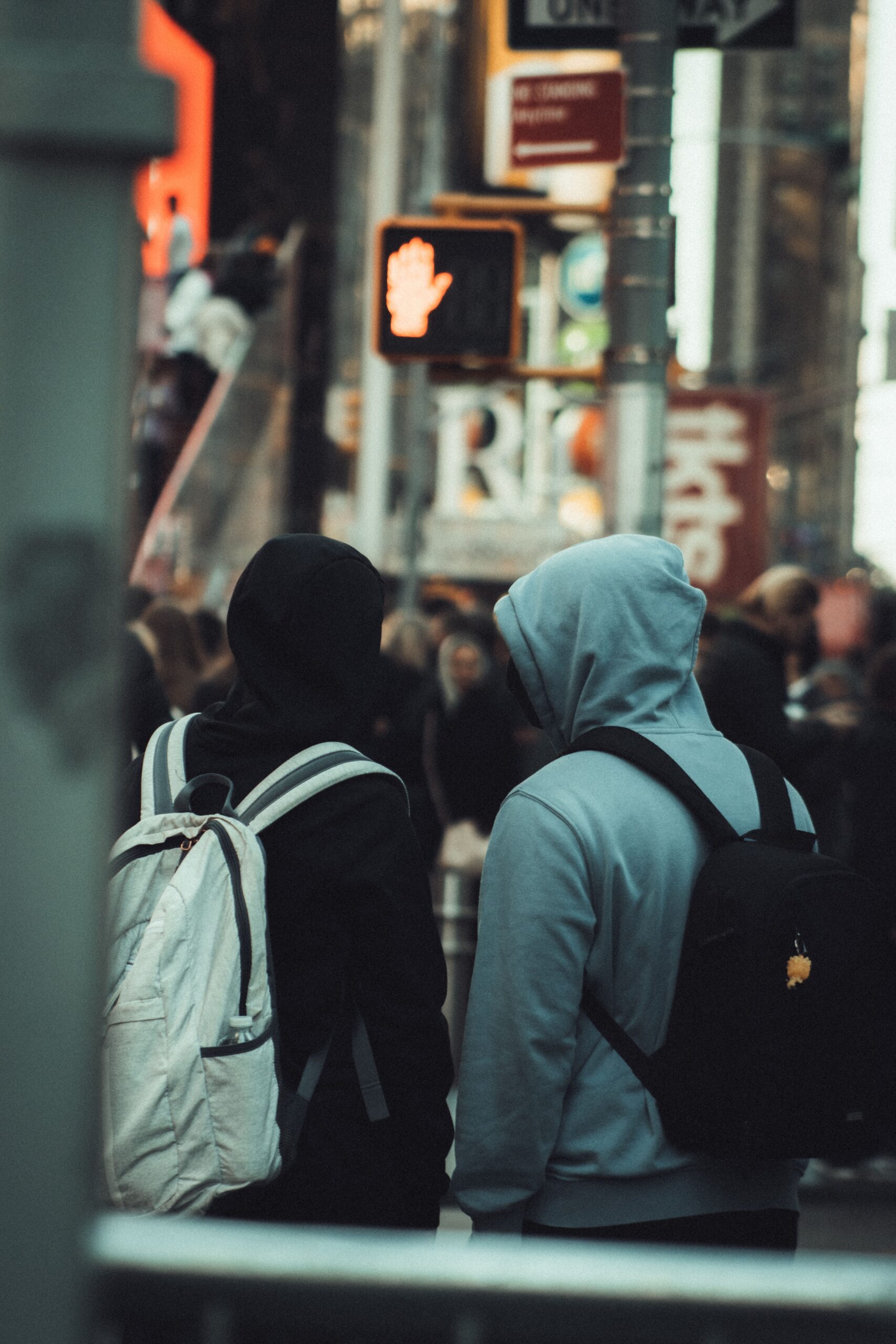 Two people carrying backpacks crossing a busy city street