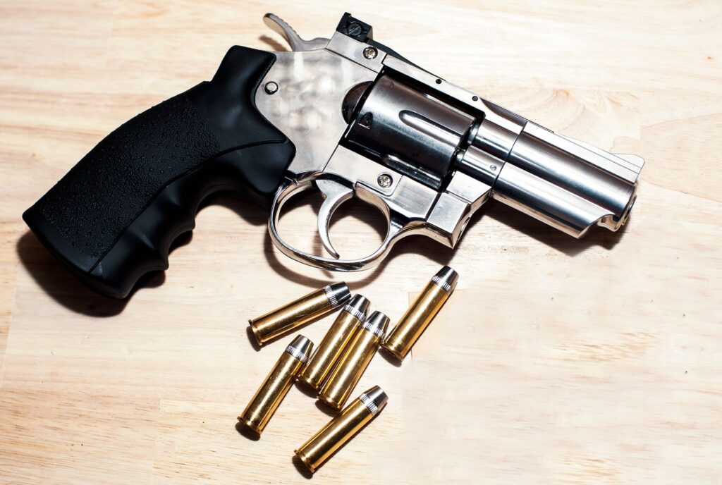 Close-up of a stainless snub-nose revolver with cartridges on a wooden table