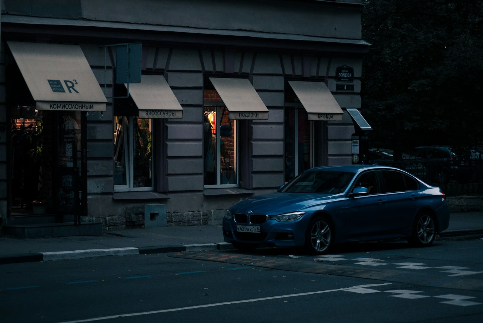 A sedan parked on a city street at dusk beside storefronts
