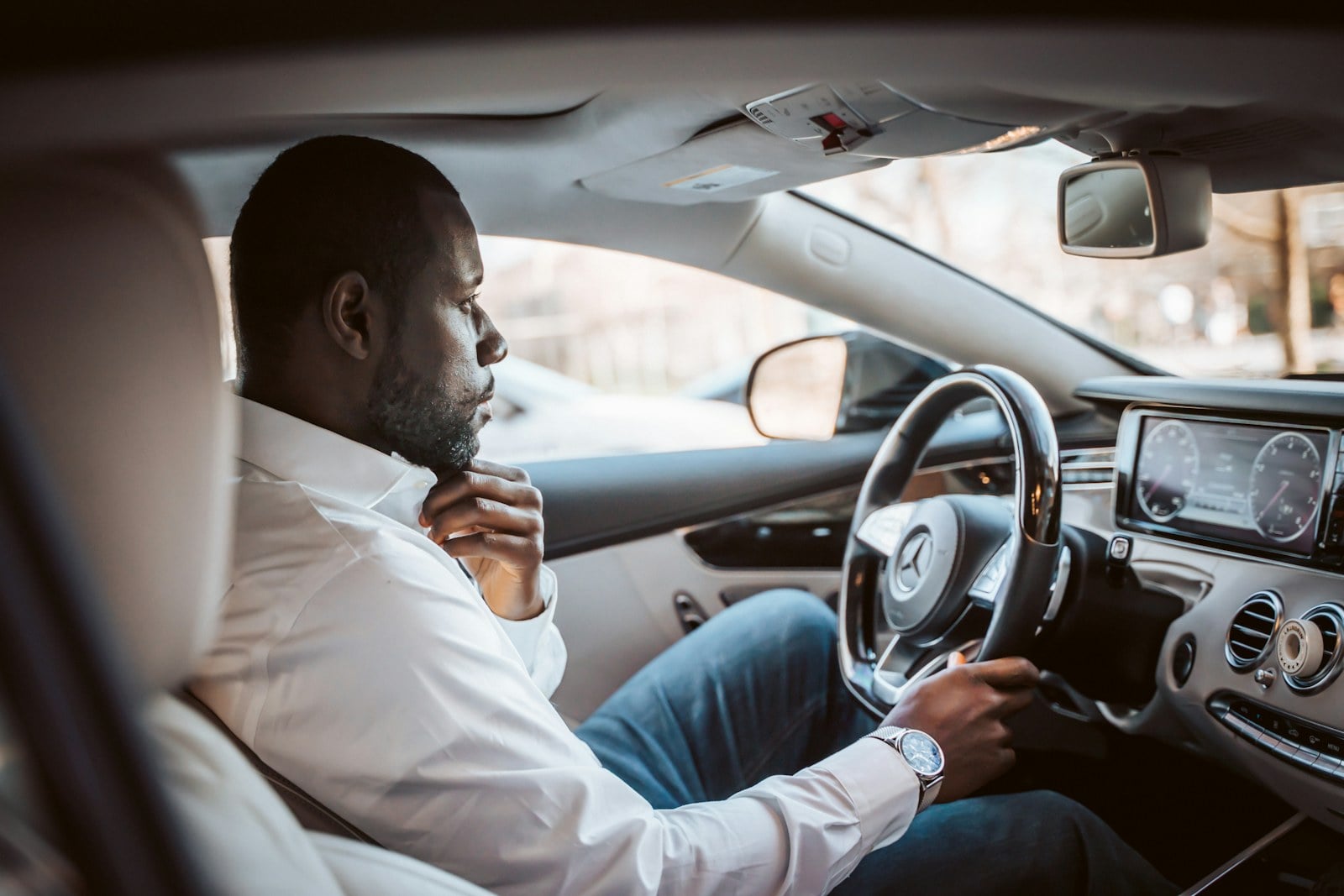 Man in a white dress shirt sitting in the driver seat with a hand on the steering wheel