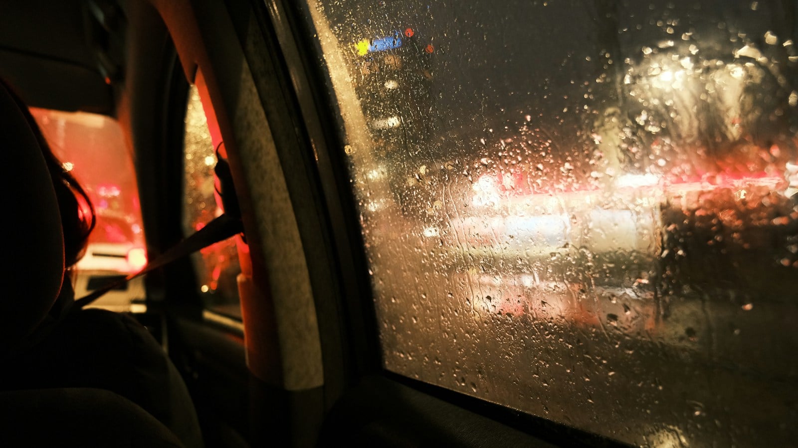 Rideshare passenger in the back seat of a car at night in the city rain